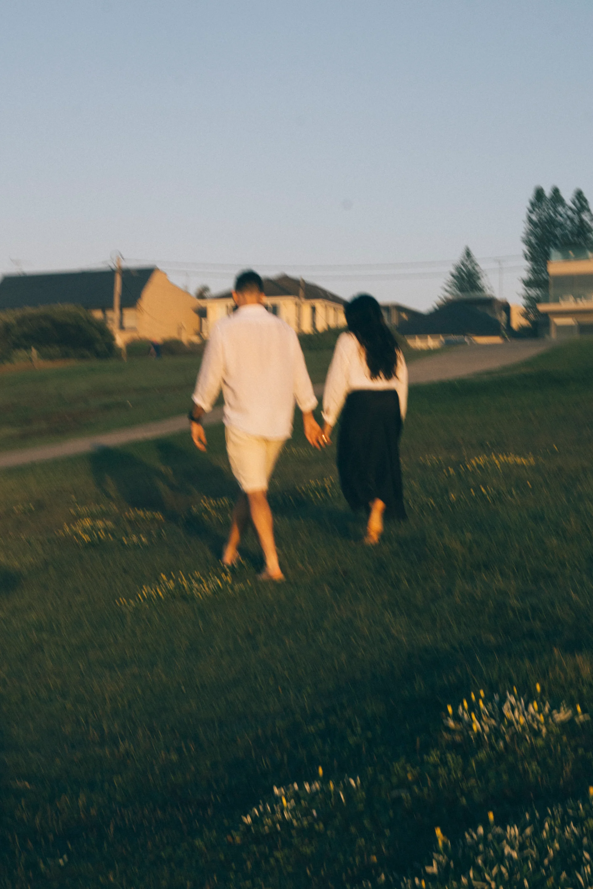 A couple walking hand in hand through golden evening light, softly blurred.