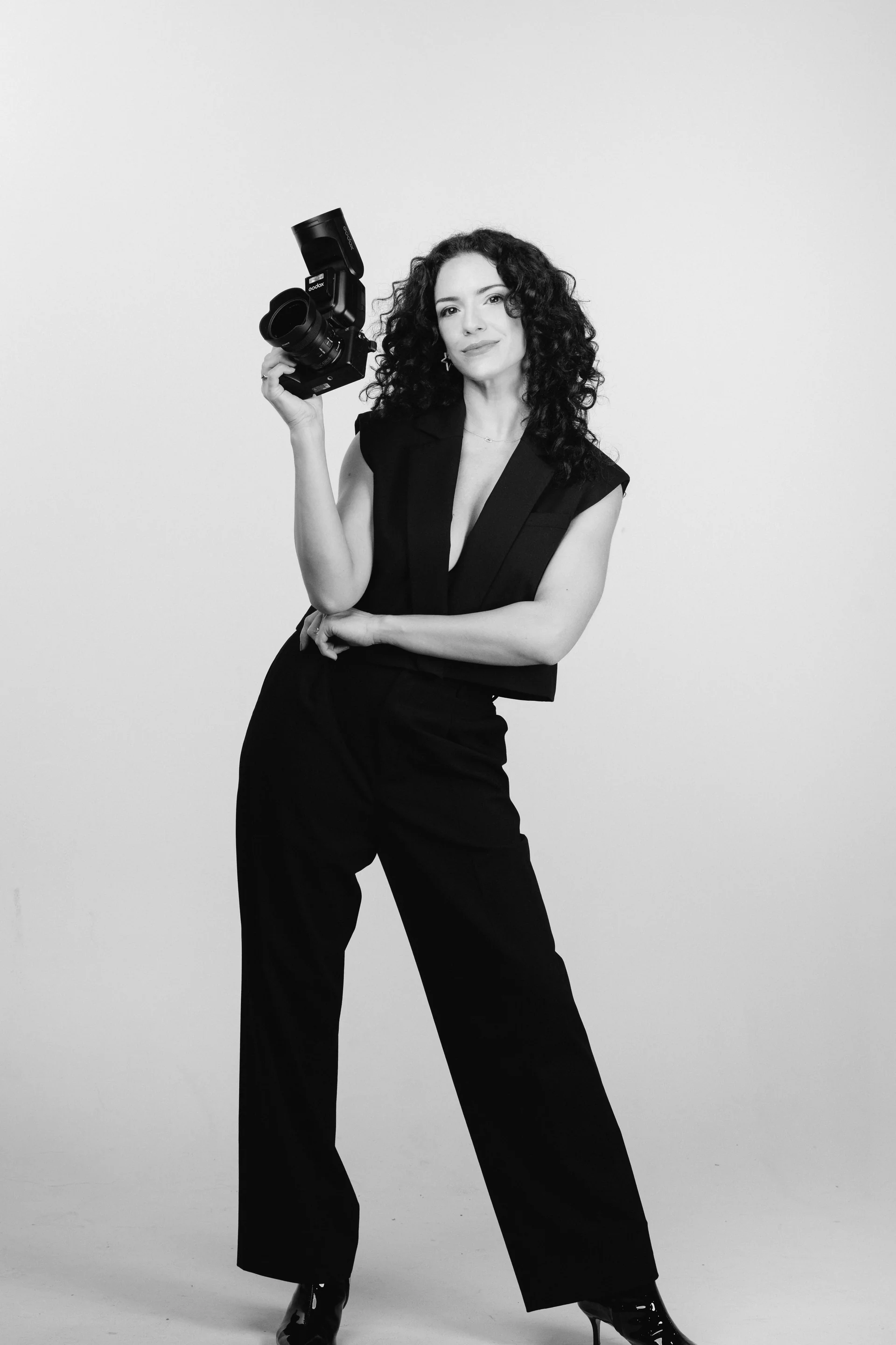Flora standing with her camera raised, in black and white.