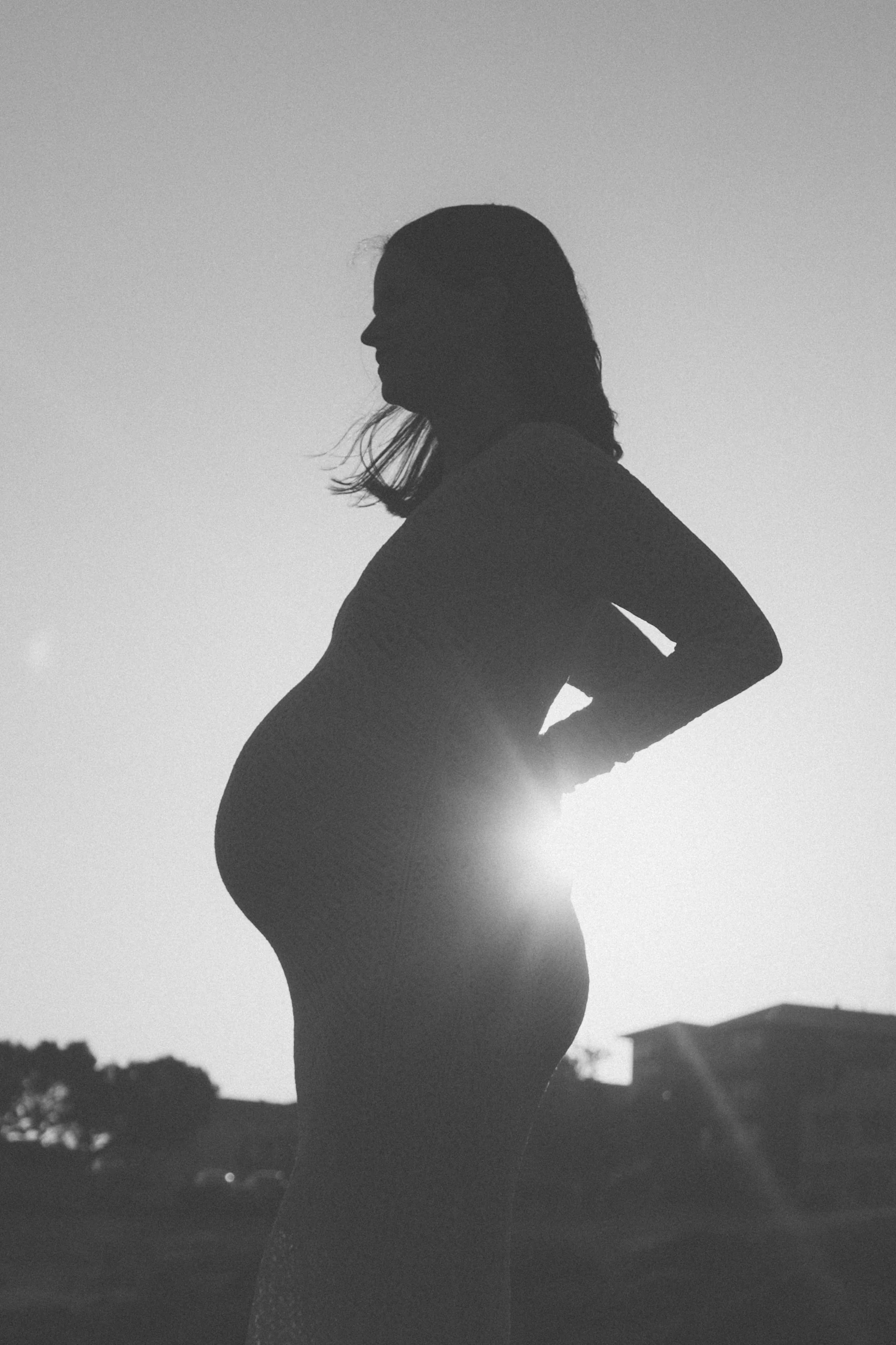 A pregnant person in a white dress, hands on her back, Sydney