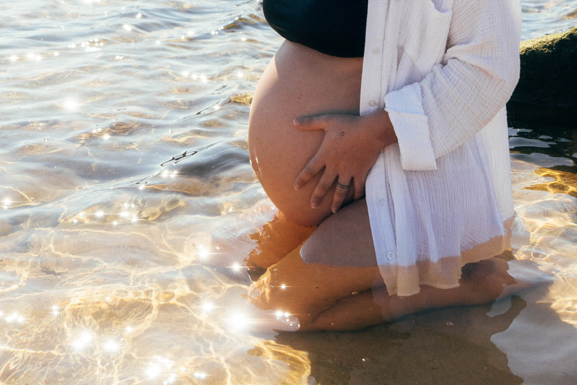 A pregnant belly cradled above sparkling golden water at a Sydney beach