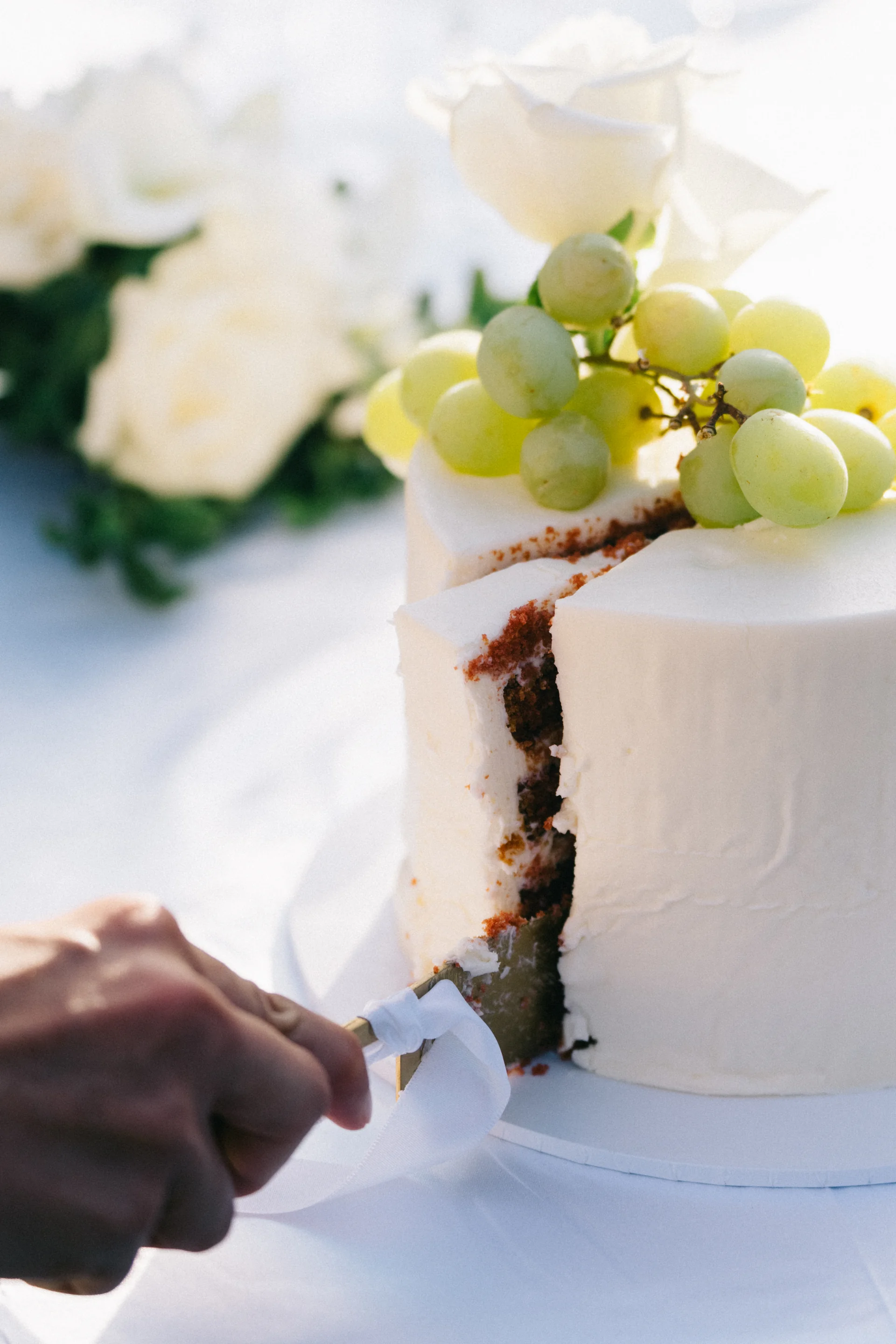 A hand cutting a white cake topped with grapes, Sydney