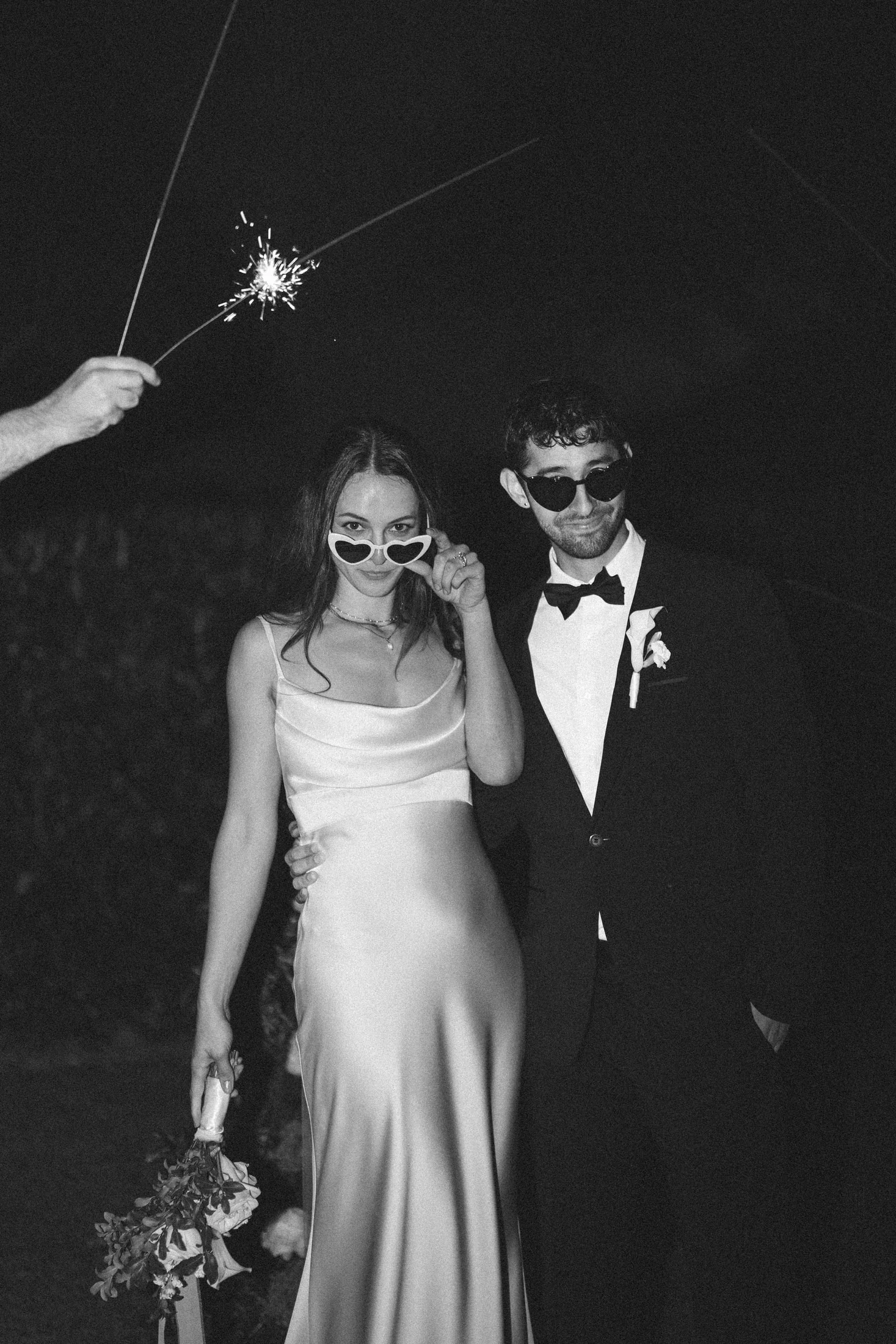 A couple in sunglasses under a sparkler, in black and white.