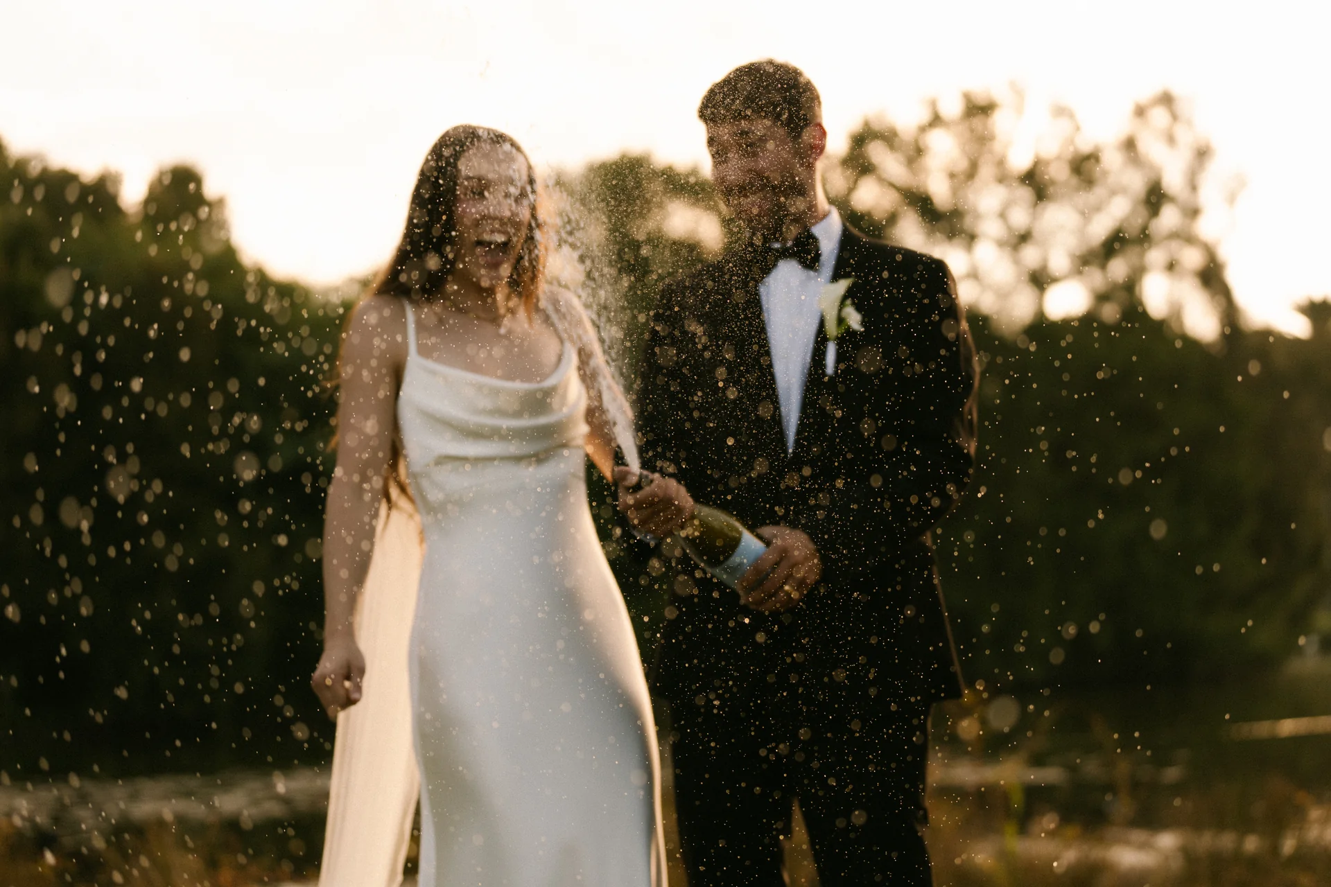 A bridal couple laughing through a champagne spray at golden hour, Sydney