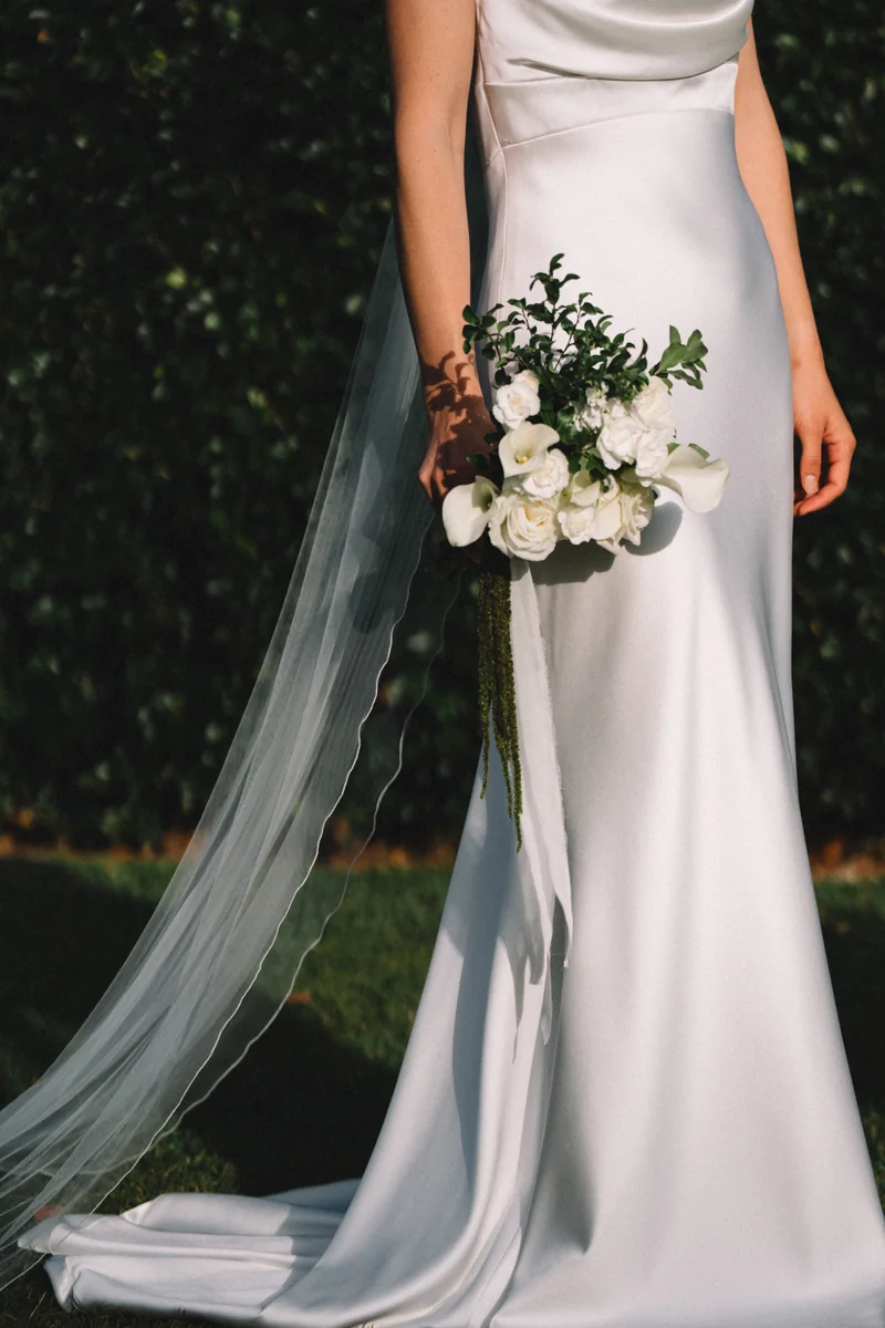 A bride holding her bouquet, veil falling to the grass